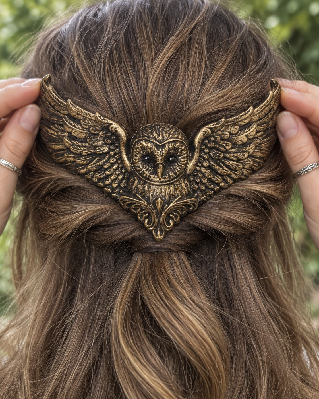 Two hands placing the Golden owl crown on a half-up twist of light-brown hair